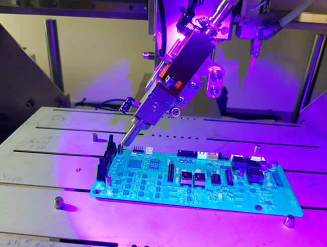 UV 조명 아래에서 코팅 로봇이 PCB를 코팅하는 모습